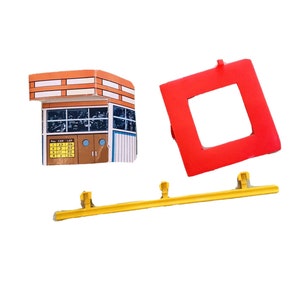 Puede incluir: Un juego de juguetes de pista de carreras vintage con una torre de control marrón y blanca, un cuadrado rojo y una barrera de pista amarilla. La torre de control tiene una lista de números y la palabra "LAP".