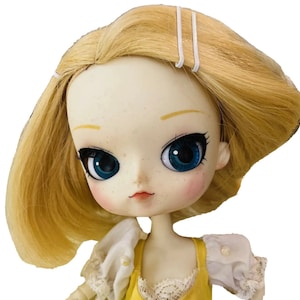 May include: A doll with blonde hair, blue eyes, and a light pink blush. She is wearing a yellow dress with white lace trim and a white blouse with a pearl button.