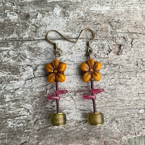 May include: A pair of dangle earrings with a flower charm, pink and green beads, and a gold-toned wire.