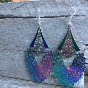 May include: A pair of iridescent earrings with a geometric design. The earrings are made of metal and have a layered, multi-dimensional look. The earrings are a vibrant mix of blue, green, purple, and pink.