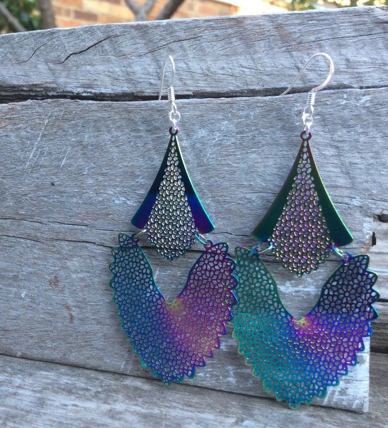 May include: A pair of iridescent earrings with a geometric design. The earrings are made of metal and have a layered, multi-dimensional look. The earrings are a vibrant mix of blue, green, purple, and pink.