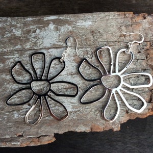 May include: A pair of silver earrings shaped like stylised flowers with open centres. The earrings are dangling and have a simple design.