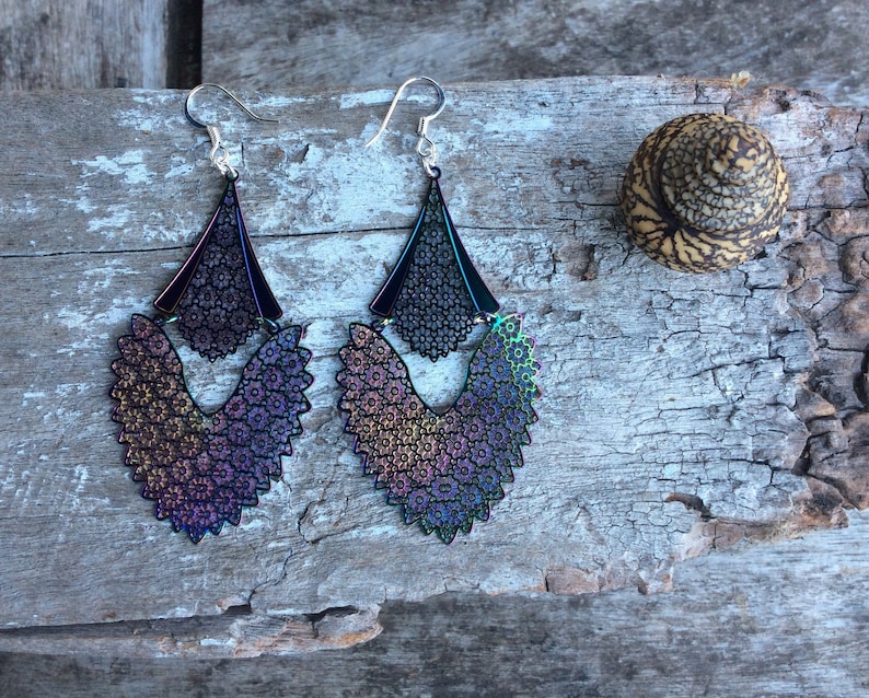May include: A pair of iridescent dangle earrings with a floral design. The earrings are silver and have a black base.