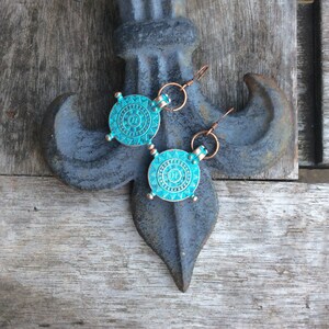 May include: A pair of turquoise blue earrings with copper accents. The earrings feature a circular design with intricate details.