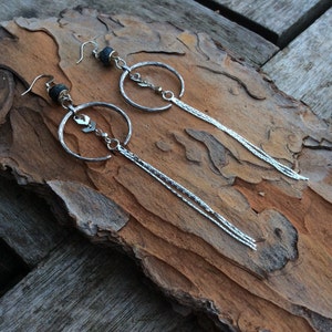 Op de afbeelding: Een paar zilveren creolen met een hangende ketting en een kleine zwarte kraal aan de bovenkant van elke creool.