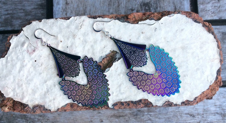 May include: A pair of iridescent black dangle earrings with a geometric design. The earrings are made of metal and have a delicate, intricate pattern.