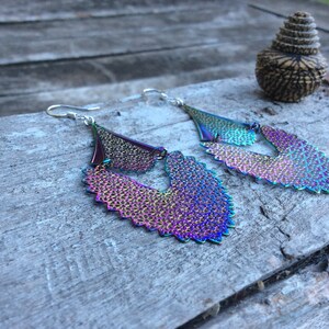 May include: A pair of iridescent earrings with a layered, scalloped design. The earrings are made of metal and have a silver tone.