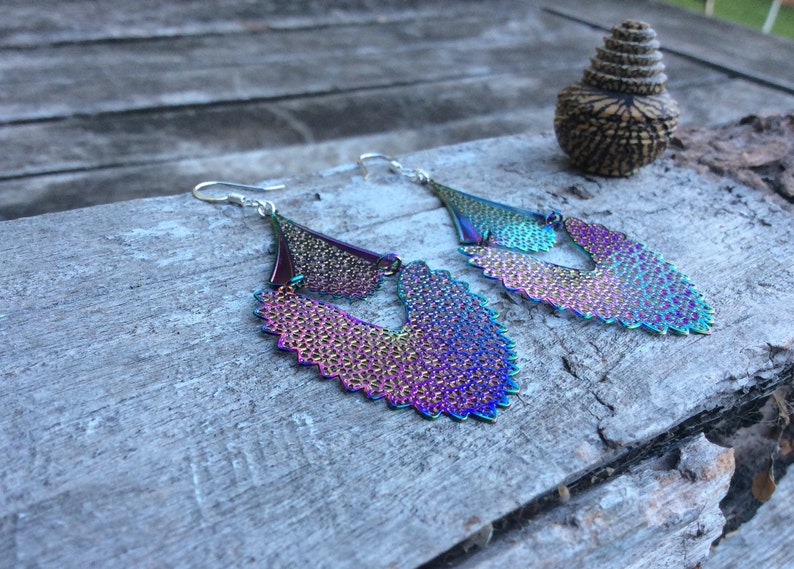 May include: A pair of iridescent earrings with a layered, scalloped design. The earrings are made of metal and have a silver tone.