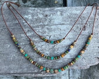 May include: Three layered necklaces with brown leather cords and colorful glass beads in shades of green, blue, gold, and brown.