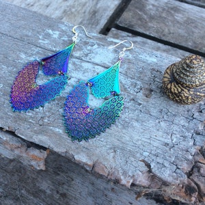 May include: A pair of iridescent earrings with a delicate, intricate design. The earrings are made of metal and have a silver tone. They are shaped like a teardrop and have a layered design.