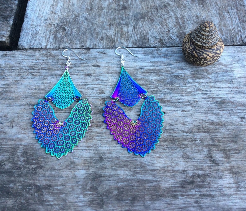 May include: A pair of iridescent blue and purple dangle earrings with a delicate, intricate design. The earrings are made of metal and have a silver-toned finish.