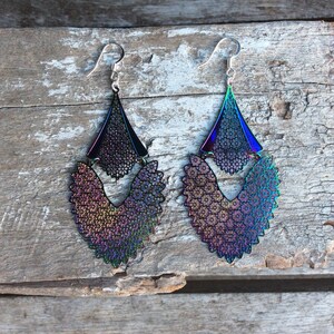 May include: A pair of iridescent earrings with a layered design. The earrings are made of metal and have a geometric shape. The earrings are a dark purple, blue, and green color.