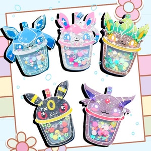 May include: Five colorful resin charms shaped like Pokemon characters in a bubble tea cup. The charms are blue, pink, green, black, and purple. Each charm has glitter and colorful sprinkles inside the cup.