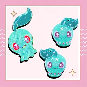 May include: Three turquoise blue and sparkly resin charms featuring cartoon characters with large eyes and pink cheeks. The charms are shaped like a jellyfish, a seahorse, and a fish.
