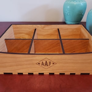 May include: A wooden organizer with six compartments and a black trim. The organizer has a curved front edge and is engraved with the initials "AAJ".