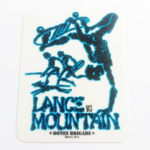 May include: A blue and black sticker with a graphic of a person skateboarding and the text "Lance Mountain" with the words "Bones Brigade" and "S.O.C. 2012" below.