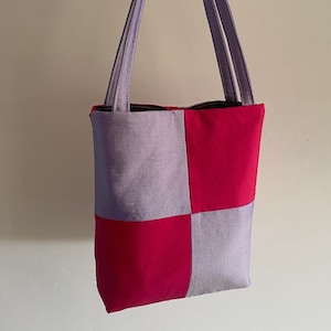 May include: A small tote bag with a checkered pattern in purple and pink. The bag has two straps.