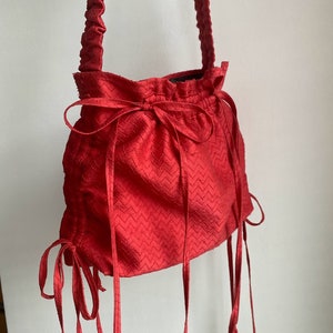 May include: A red drawstring bag with a ruffled top and long ties. The bag has a textured, chevron pattern.