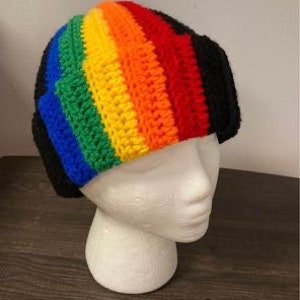 May include: A rainbow crochet beanie with a black brim. The beanie is made with a variety of colours, including red, orange, yellow, green, blue, and purple.