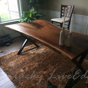 May include: A large, live edge wood table with a dark brown finish and black metal legs. The table is set with two white candles in glass holders.