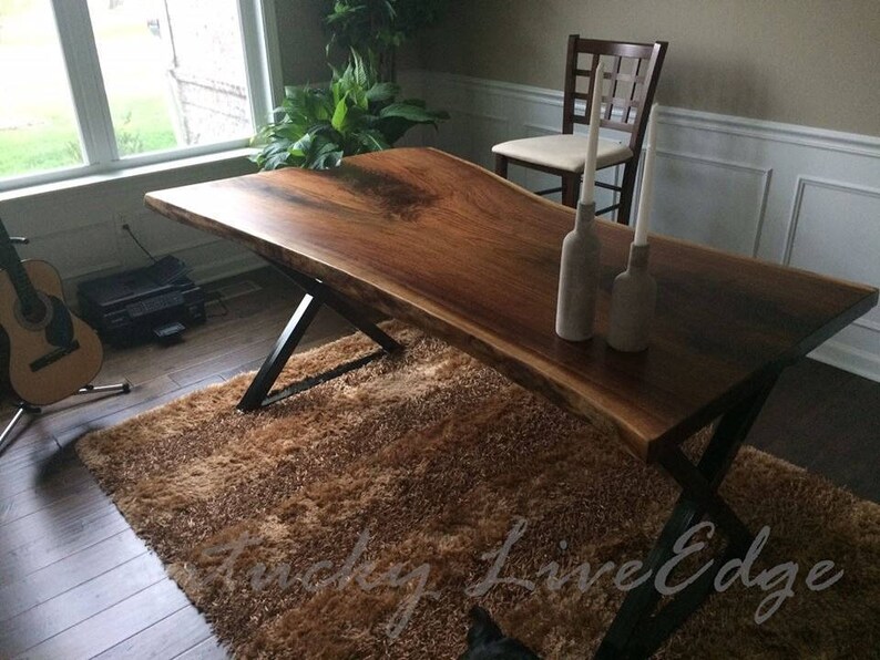 May include: A large, live edge wood table with a dark brown finish and black metal legs. The table is set with two white candles in glass holders.