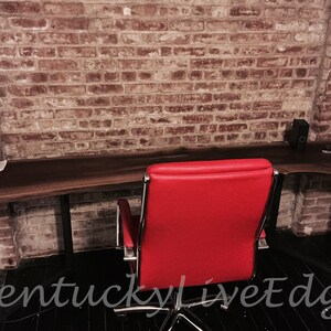 May include: A dark wood live edge desk with black metal legs and a red office chair. The desk is in front of a brick wall.