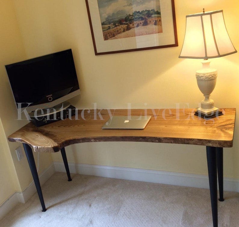 May include: A wooden desk with a live edge top and black metal legs. A laptop computer and a lamp are on the desk.