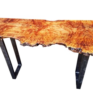 May include: A live edge wood console table with a natural wood finish and a unique, irregular shape. The table has a black metal frame with two legs on each side. The table is made by Kentucky Live Edge.
