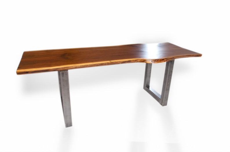 May include: A long, rectangular wooden table with a live edge top and a natural wood finish. The table has two metal legs with a square design.