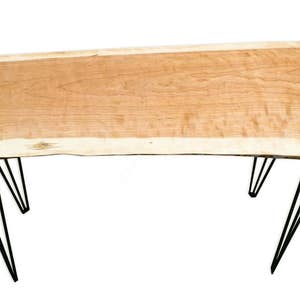 May include: A wooden table with a live edge top and black hairpin legs. The table top is made of natural wood with a light brown color and a unique grain pattern.
