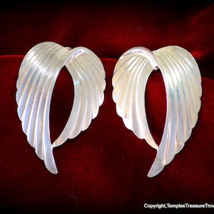 May include: A pair of silver earrings shaped like wings. The earrings are made of smooth, shiny metal and have a delicate, feminine design.