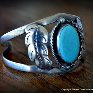 Puede incluir: Una pulsera de plata con una piedra turquesa y dise&ntilde;os de plumas. La pulsera est&aacute; abierta y tiene un dise&ntilde;o simple.