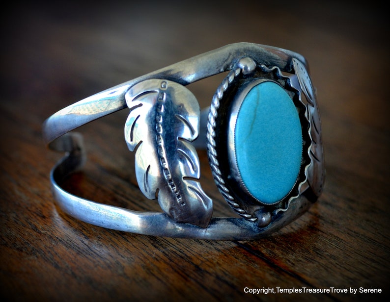 Puede incluir: Una pulsera de plata con una piedra turquesa y dise&ntilde;os de plumas. La pulsera est&aacute; abierta y tiene un dise&ntilde;o simple.