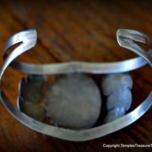 Puede incluir: Un brazalete de plata con una piedra grande, redonda y de color turquesa engastada en el centro. El brazalete est&aacute; decorado con piedras turquesa m&aacute;s peque&ntilde;as y detalles de plata.