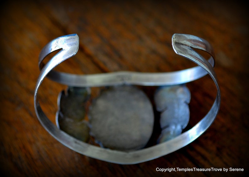 Puede incluir: Un brazalete de plata con una piedra grande, redonda y de color turquesa engastada en el centro. El brazalete est&aacute; decorado con piedras turquesa m&aacute;s peque&ntilde;as y detalles de plata.