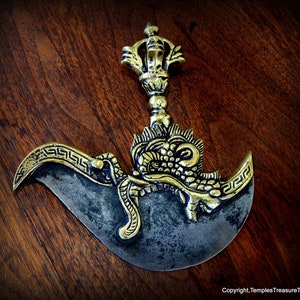 May include: A gold-colored metal ceremonial knife with a dragon design and a curved blade. The handle is decorated with a stylized floral design and a finial.