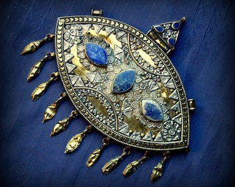 May include: A silver and gold pendant with a geometric design and three blue stones. The pendant has a fringe of small gold beads.