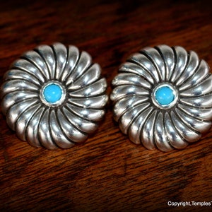 Könnte beinhalten: Ein Paar silberne Ohrringe mit einem Türkis-Stein in der Mitte jedes Ohrrings. Die Ohrringe sind rund und haben ein Spiraldesign.