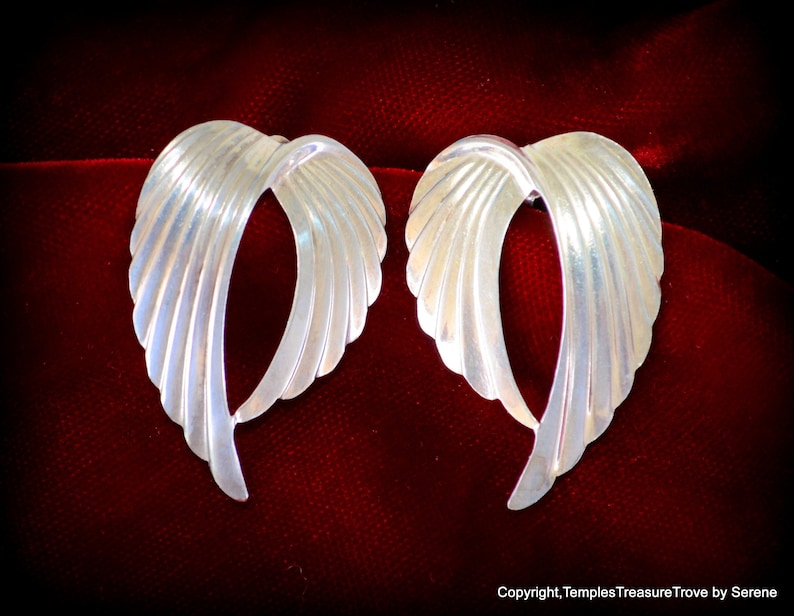 May include: A pair of silver earrings shaped like wings. The earrings are made of smooth, shiny metal and have a delicate, feminine design.
