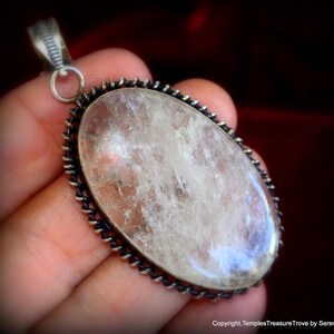 May include: A silver pendant with a large, clear, oval-shaped quartz crystal set in a silver bezel. The bezel has a decorative, twisted wire design.