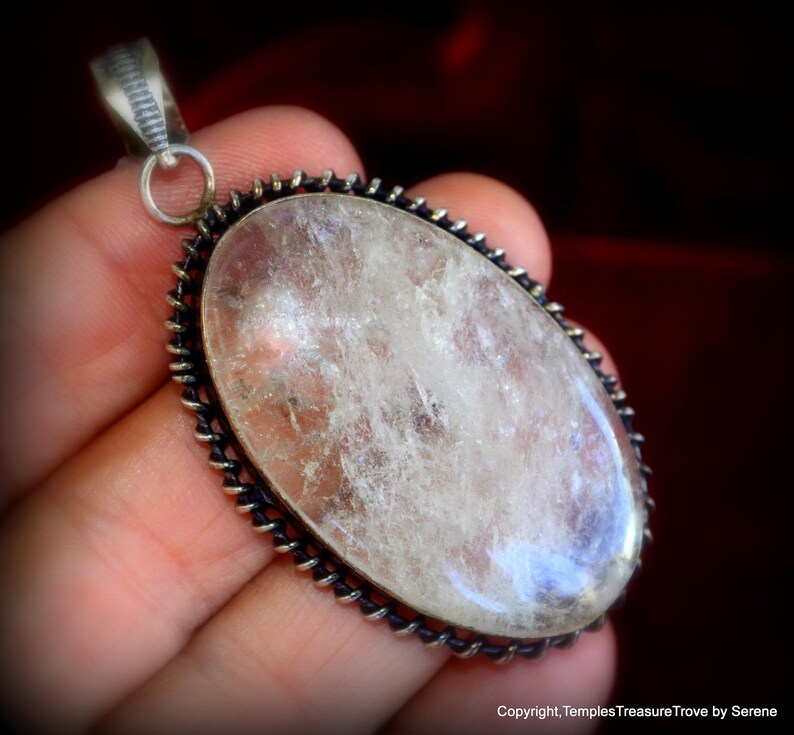 May include: A silver pendant with a large, clear, oval-shaped quartz crystal set in a silver bezel. The bezel has a decorative, twisted wire design.