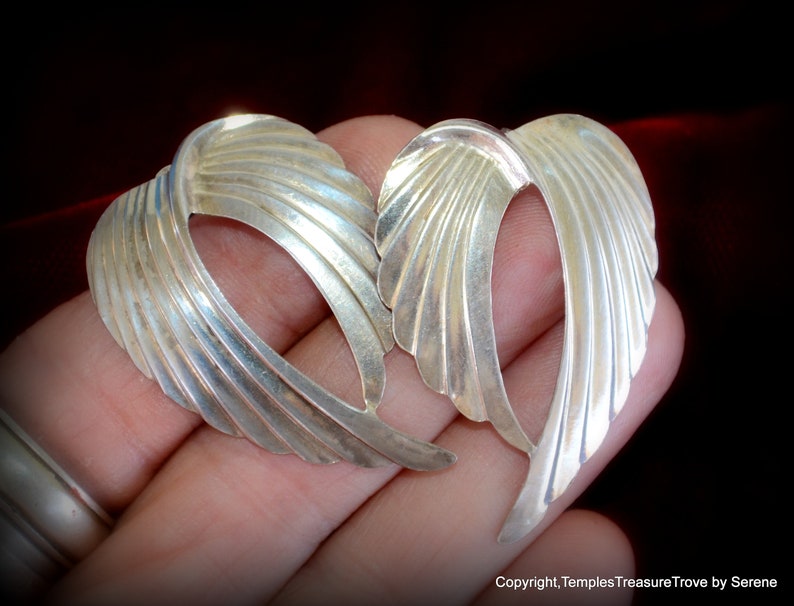 May include: A pair of silver earrings shaped like wings. The earrings are made of smooth, textured metal and have a delicate, feminine design.