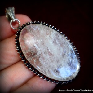 May include: A silver pendant with a clear quartz crystal set in a silver bezel. The pendant has a detailed, ornate design around the edge.