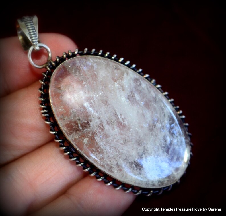 May include: A silver pendant with a clear quartz crystal set in a silver bezel. The pendant has a detailed, ornate design around the edge.
