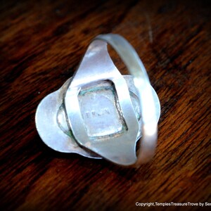 May include: Silver ring with a square-shaped stone set in a silver frame. The back of the ring has the word "TRUN" engraved on it.