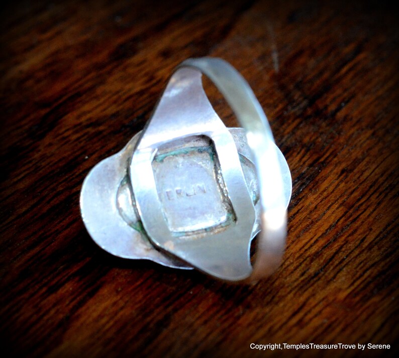 May include: Silver ring with a square-shaped stone set in a silver frame. The back of the ring has the word "TRUN" engraved on it.