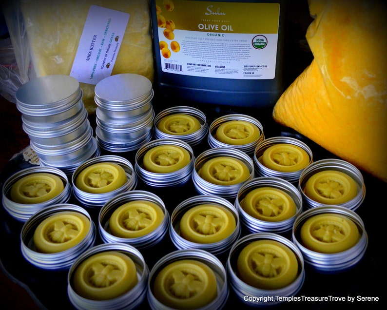 May include: A close-up of 17 small round metal tins filled with a yellow substance. The tins are arranged in rows on a black surface. The tins have a bee design on the top.