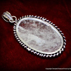 May include: A silver pendant with a clear quartz crystal set in a twisted wire frame. The pendant is oval shaped and has a silver bail.