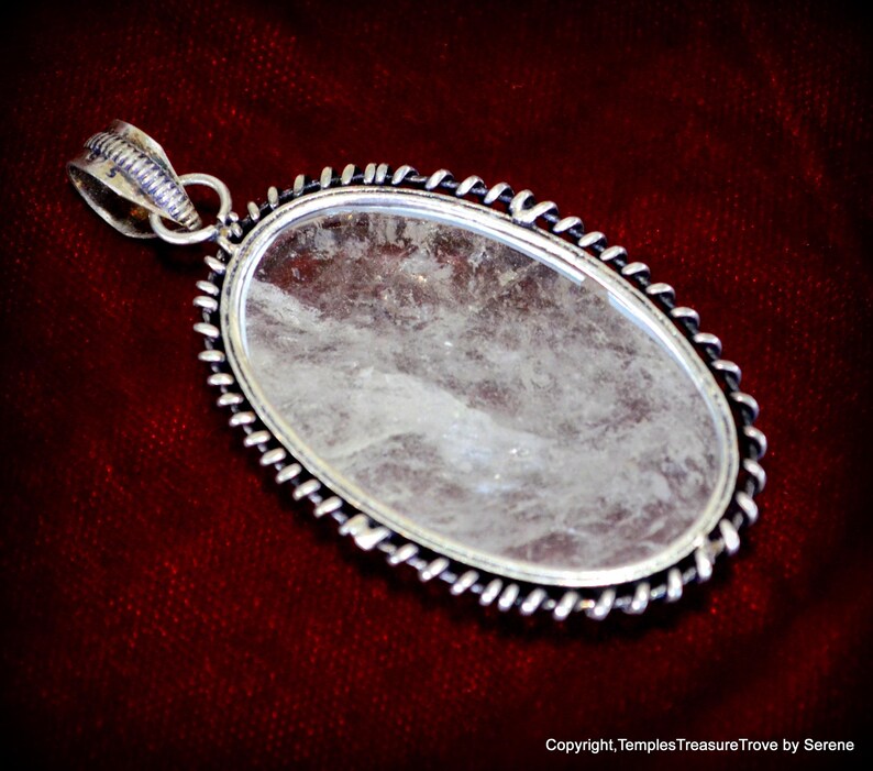 May include: A silver pendant with a clear quartz crystal set in a twisted wire frame. The pendant is oval shaped and has a silver bail.