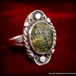 May include: A silver ring with a green stone set in an oval bezel. The ring has a twisted band and decorative accents around the stone.
